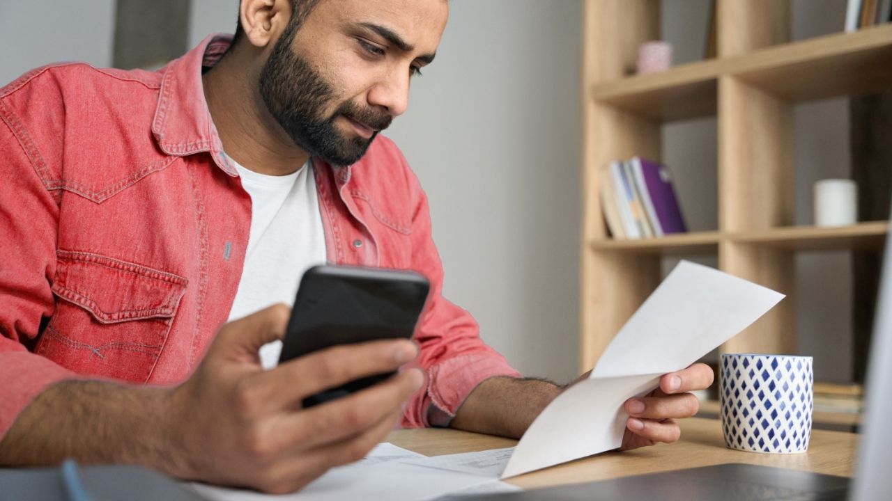 senhor com telemóvel na mão e a olhar para um documento